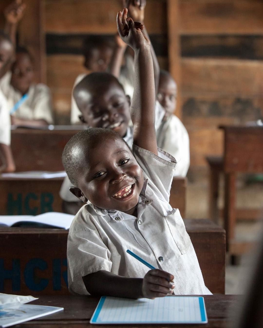A smiling student raising his hand to answer in class